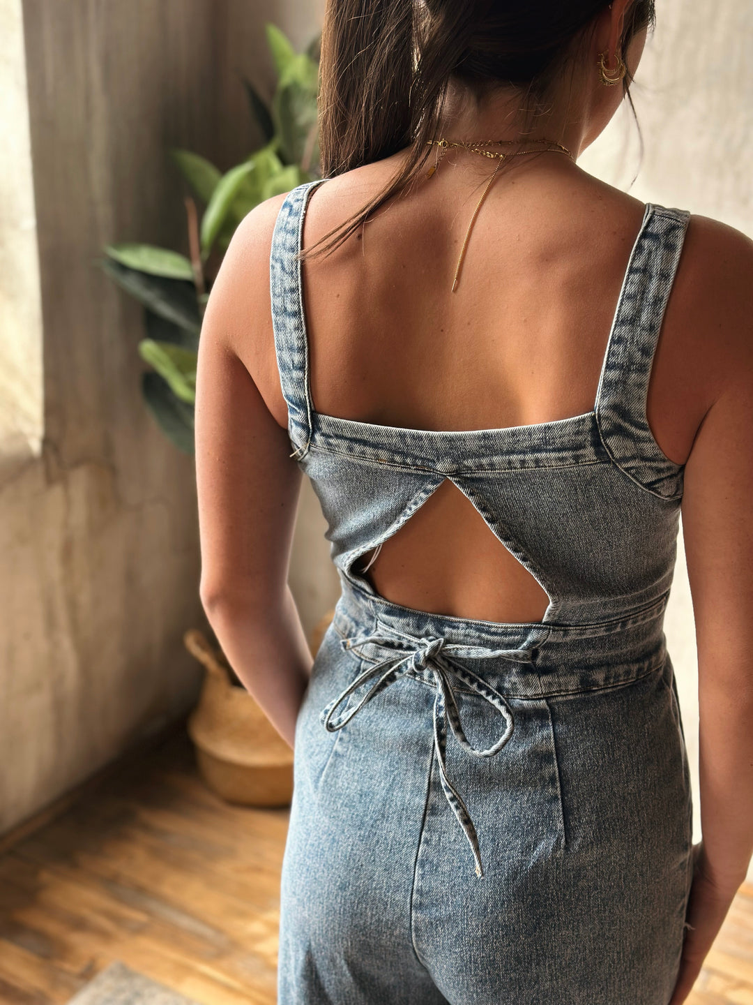 Person wearing a denim jumpsuit with cut-out design, standing indoors.