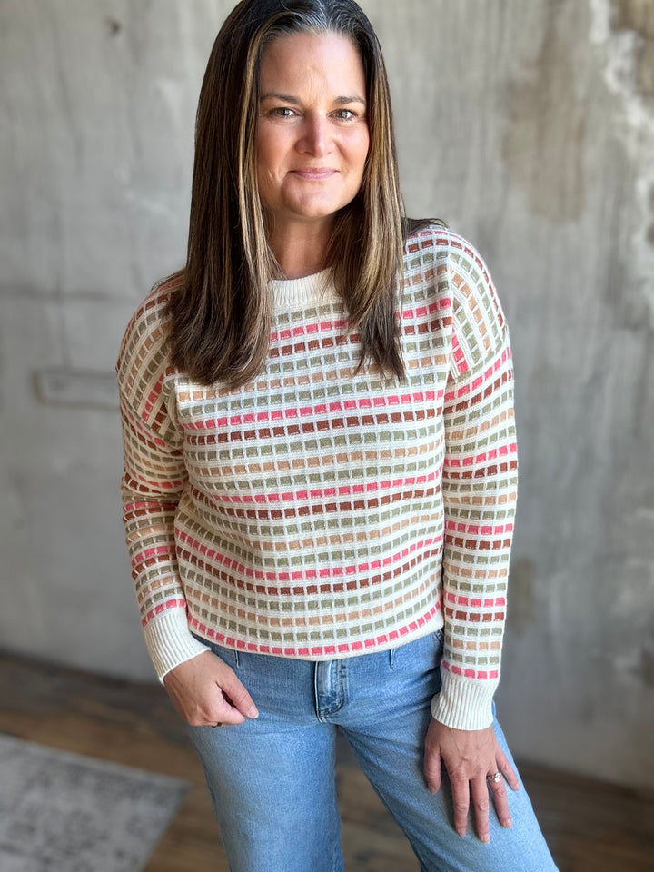 Woman wearing a cream crewneck sweater with pink, green and red stripes, front view
