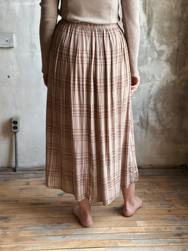 Person wearing a plaid skirt standing in a room with wooden floor and textured walls.