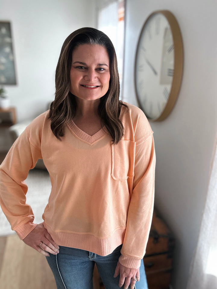 Woman wearing a peach sweater standing in a room with a clock on the wall.