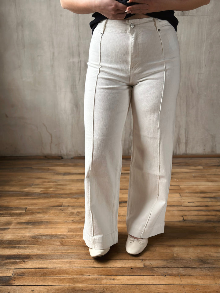 Person wearing white jeans standing on a wooden floor with a plain wall background
