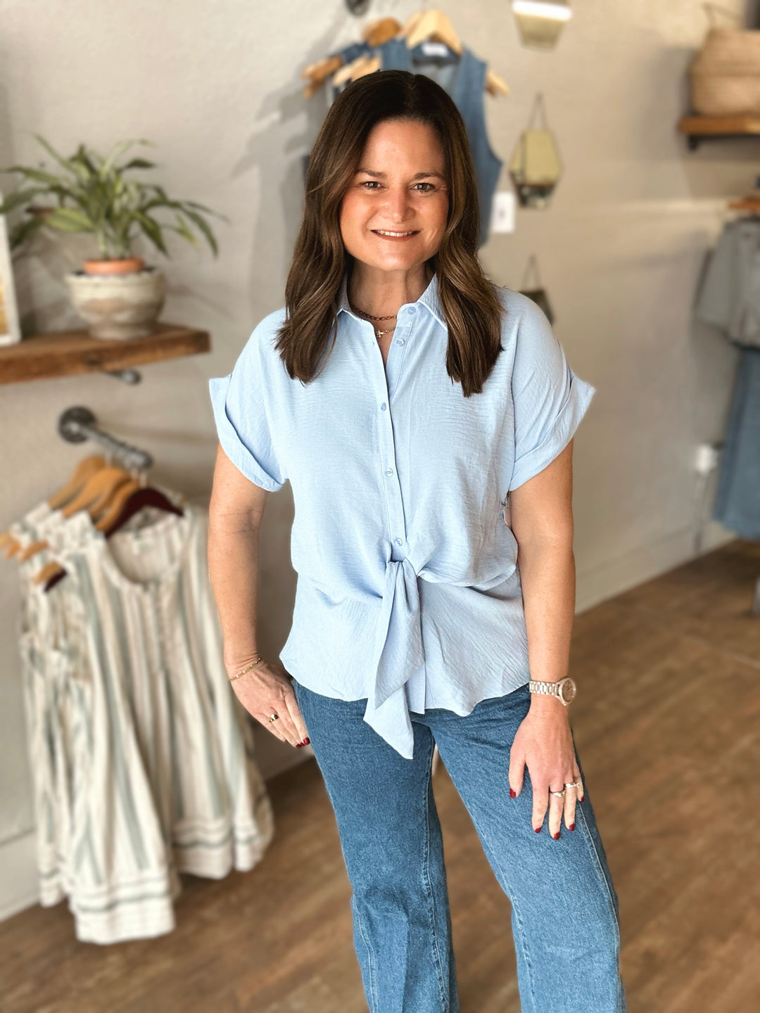 Woman wearing a light blue shirt with a tie front and jeans in a clothing store.