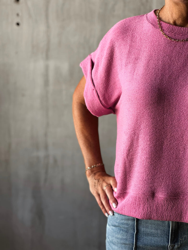 Person wearing a pink sweater against a gray concrete wall