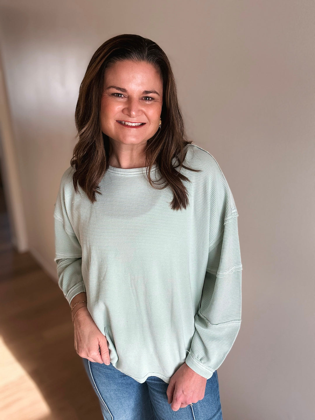 Woman wearing a light green sweater and blue jeans indoors.