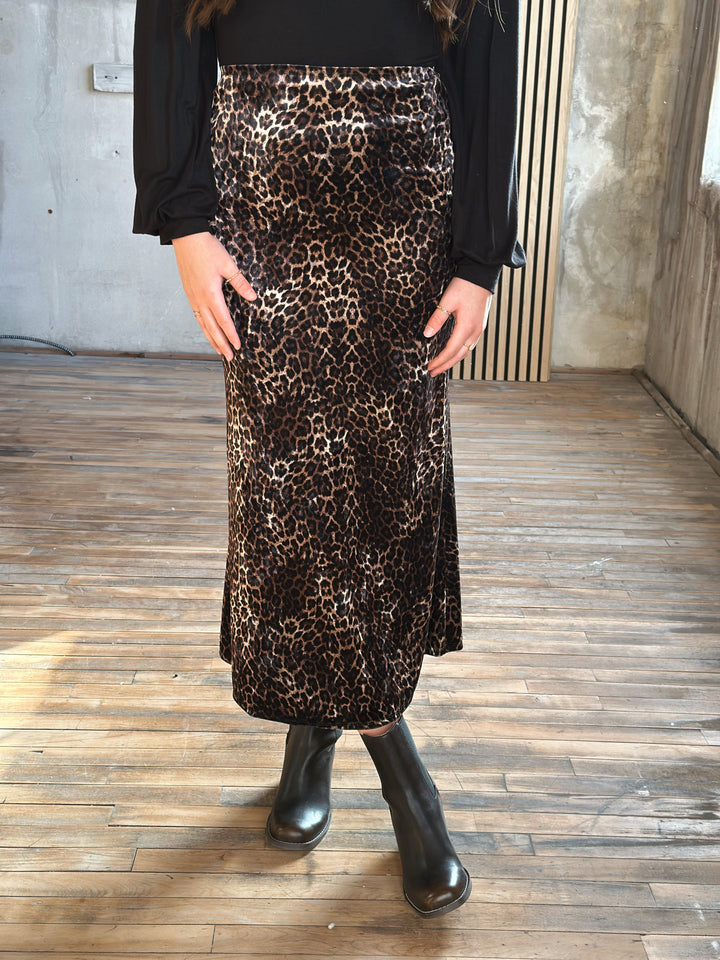 Person wearing a leopard print skirt and black boots on a wooden floor.