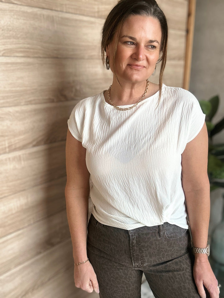 Woman wearing a white top and dark pants standing against a textured wall.