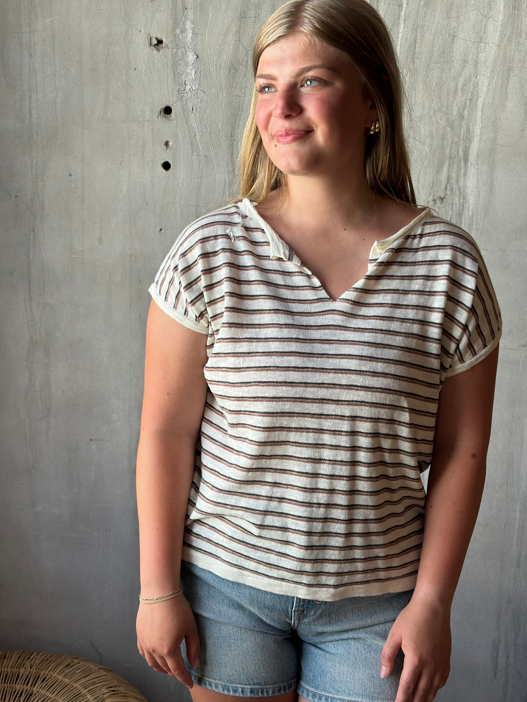 A person wearing a white and brown striped v-neck shirt and jeans on a gray floor.