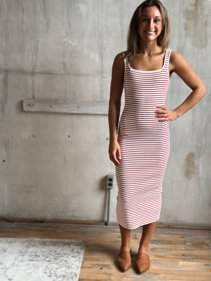Woman wearing a red and white striped dress standing against a concrete wall.