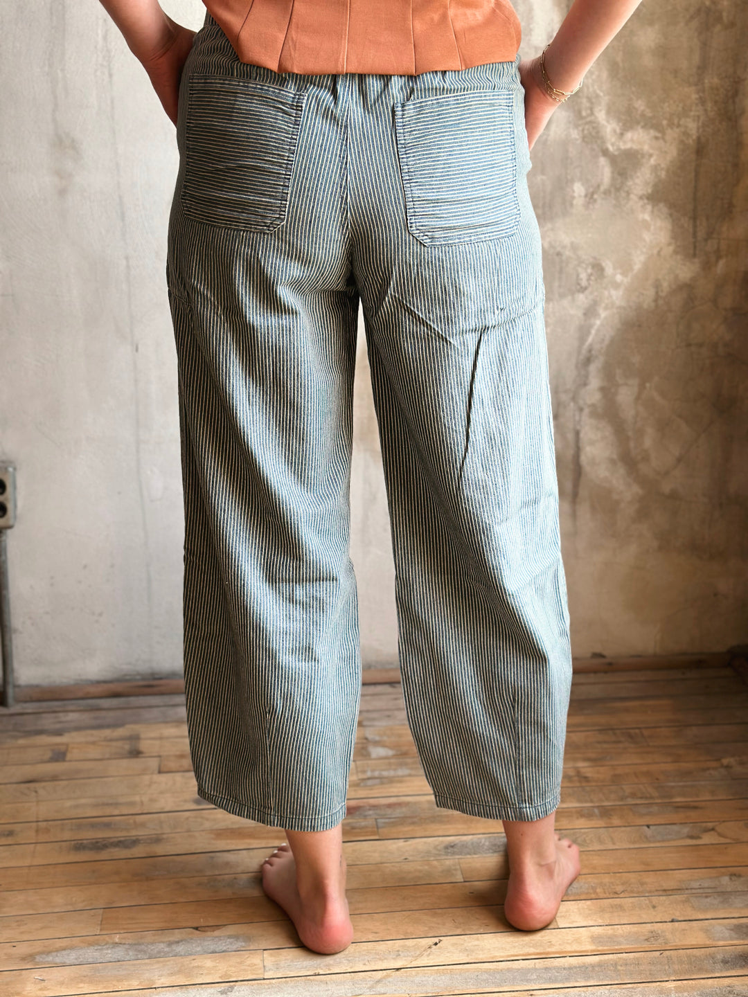 Person wearing light blue striped pants standing against a textured wall.