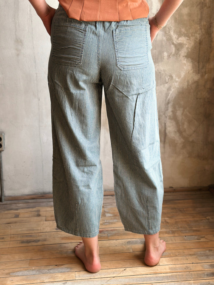 Person wearing light blue striped pants standing against a textured wall.