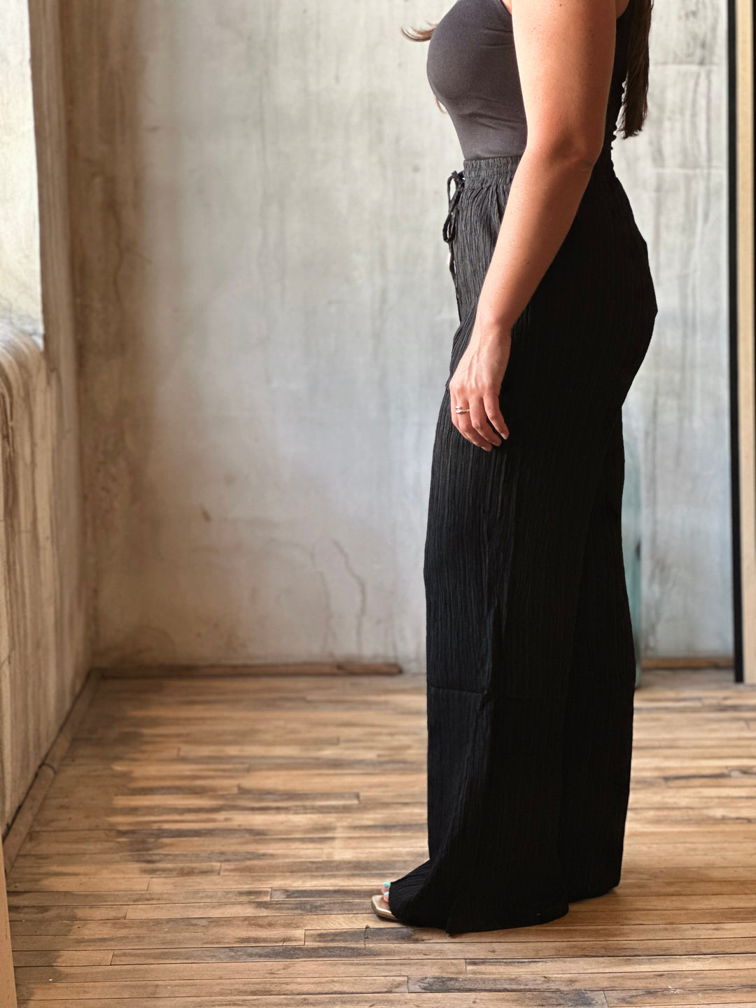 Person wearing a black dress standing in a room with wooden flooring and a textured wall.