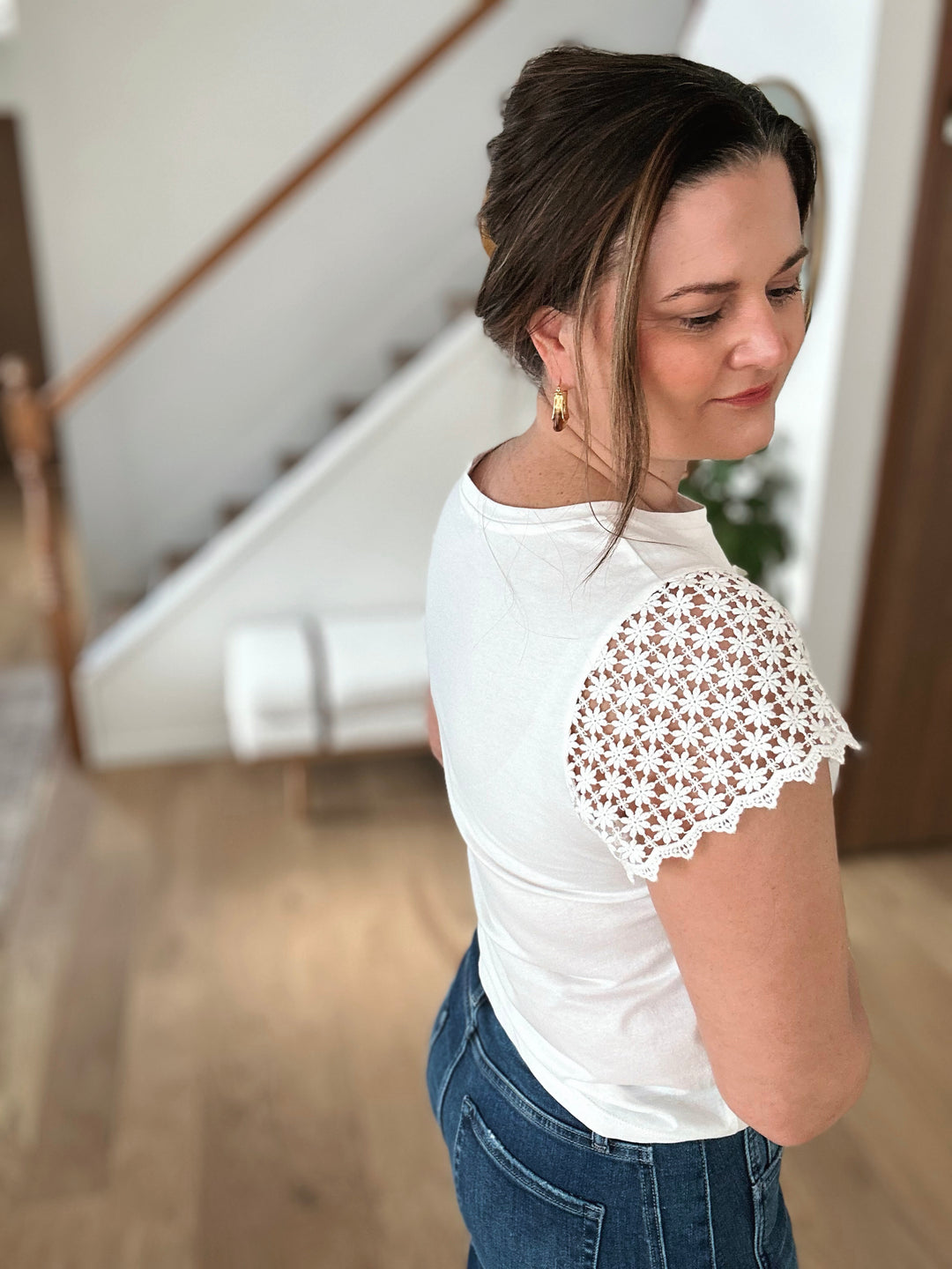 Woman wearing a white t-shirt with lace sleeves in a home setting