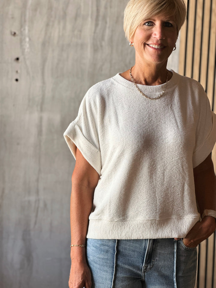 Woman wearing a white sweater and blue jeans standing against a concrete wall.