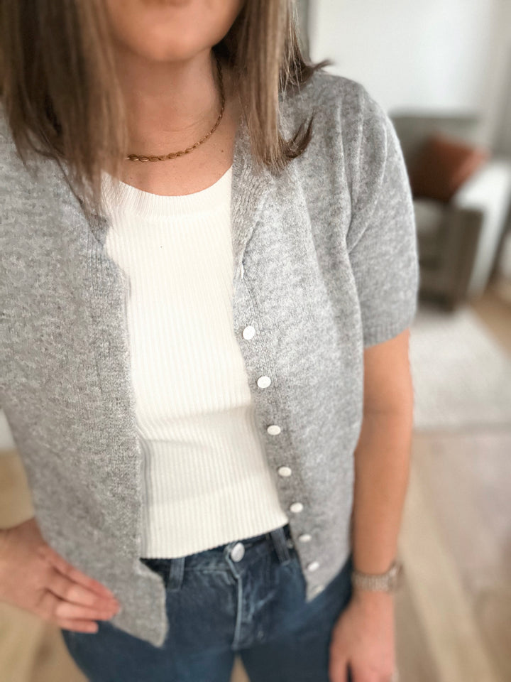 Person wearing a gray cardigan over a white shirt and blue jeans indoors.