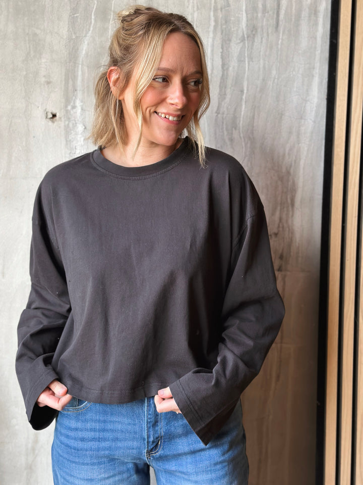 Woman wearing a dark gray sweatshirt and blue jeans against a wooden wall.