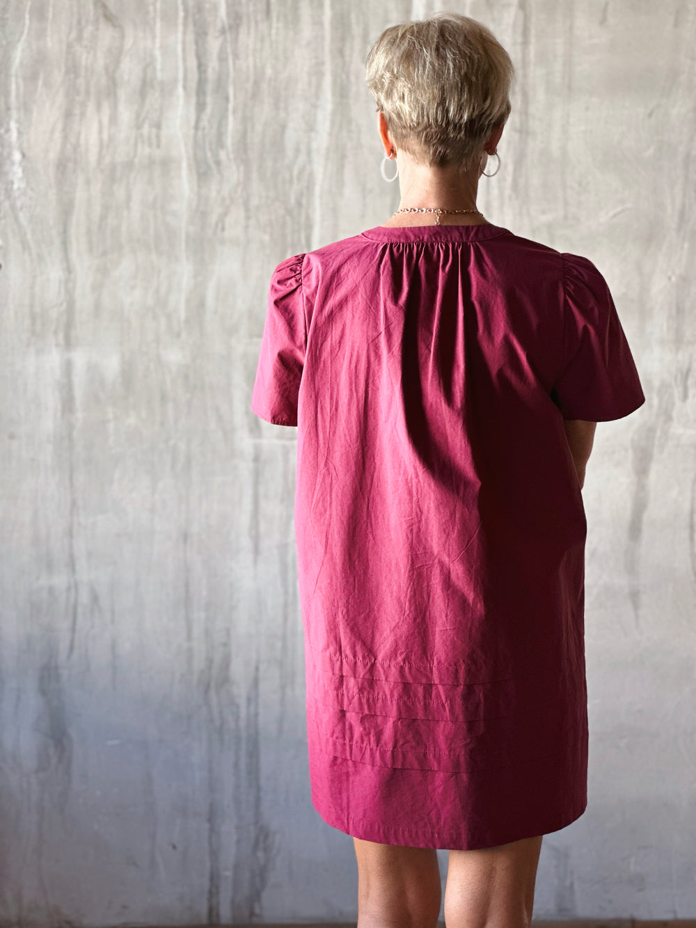 back view of mini dress features a flattering pleated bodice and voluminous poplin puff sleeves. Deep Plum. 