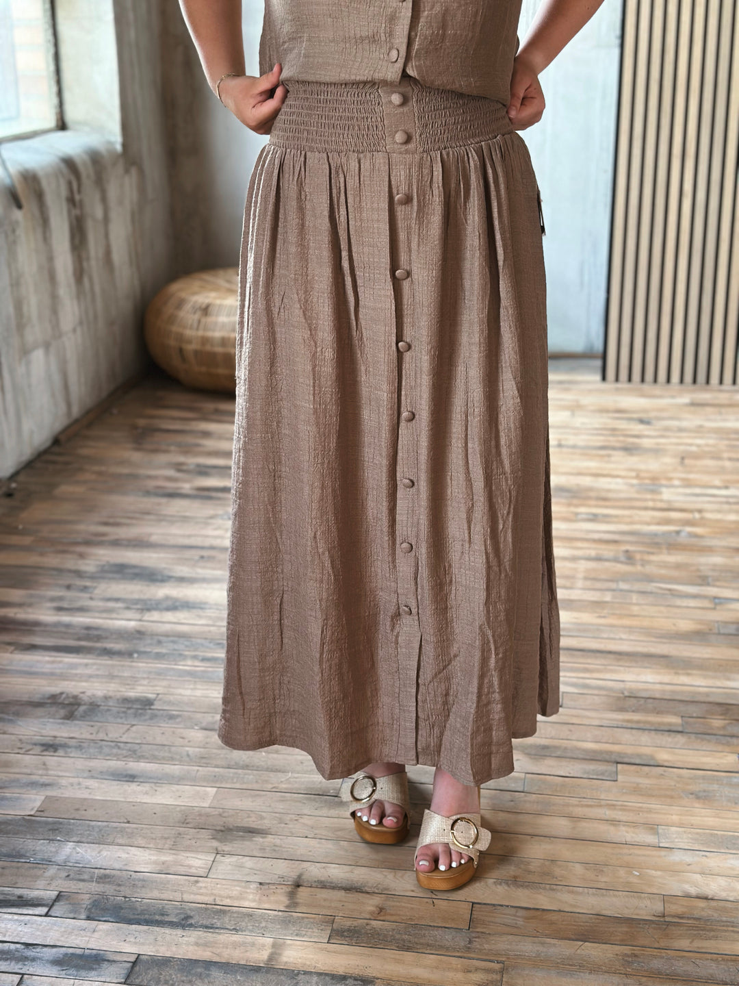 A person wearing a brown button-up skirt standing on a wooden floor.