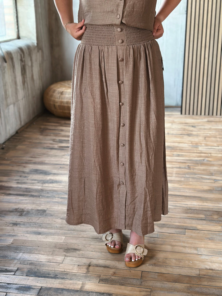 A person wearing a brown button-up skirt standing on a wooden floor.