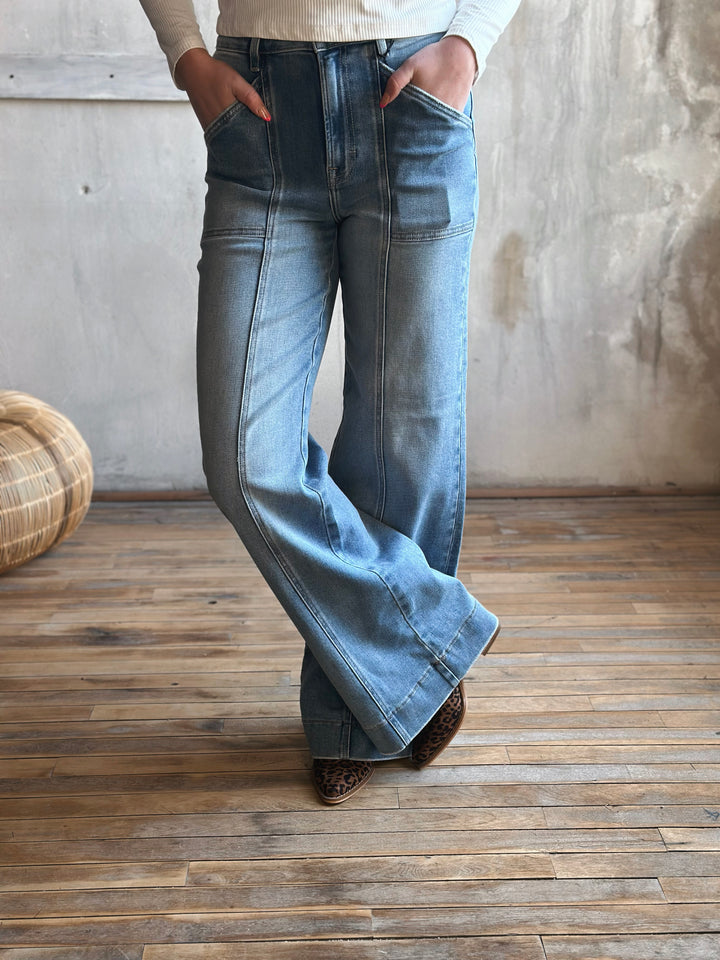 A person wearing blue flared jeans with a seam down the middle of the pants legs.