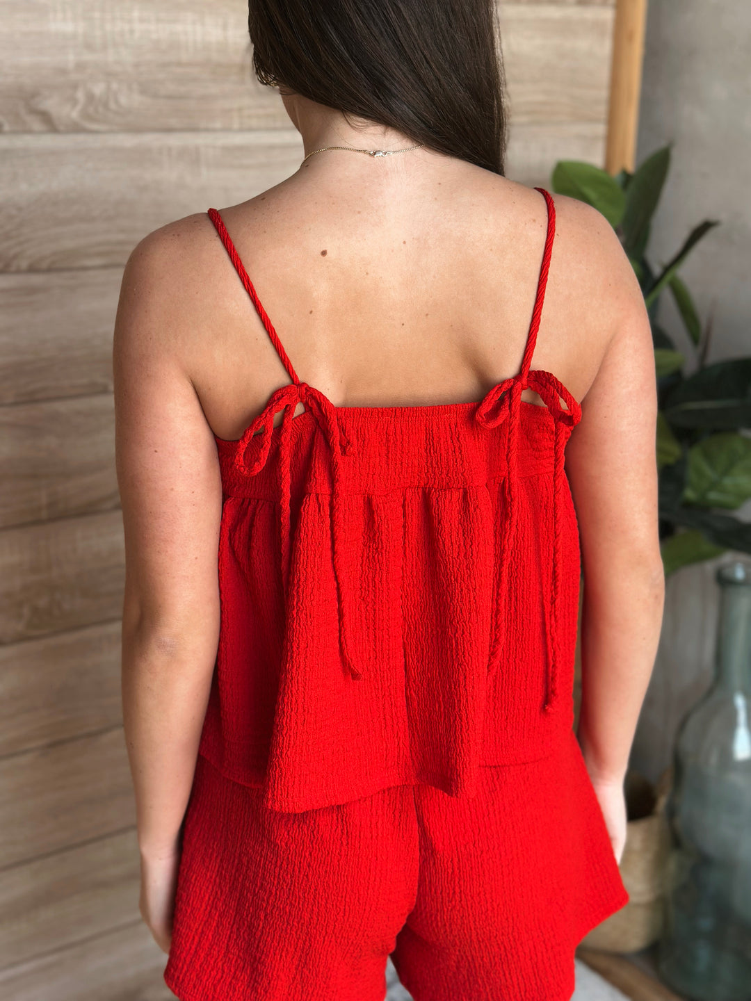Person wearing a red top with thin straps in a casual setting.