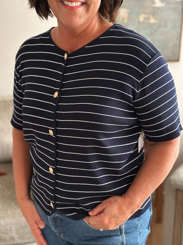 Person wearing a navy and white striped shirt with buttons, standing indoors.