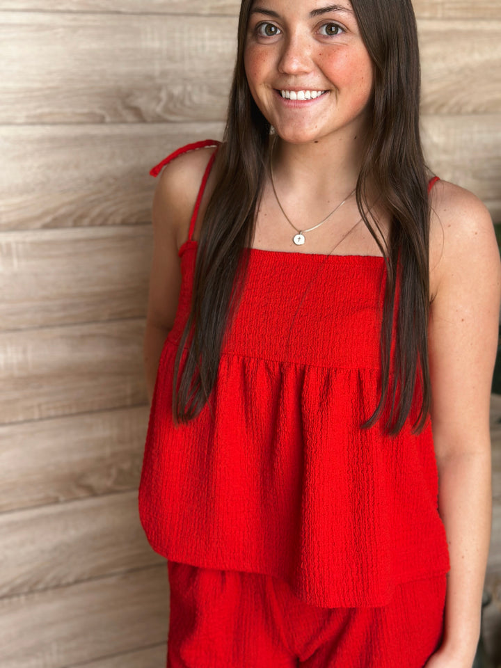 Woman wearing a red top against a wooden paneled background.