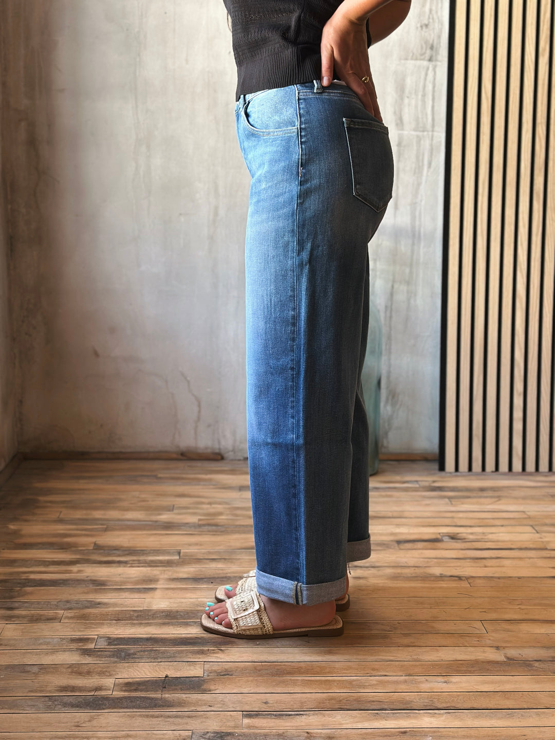 Person wearing blue jeans standing on a wooden floor with a neutral wall background