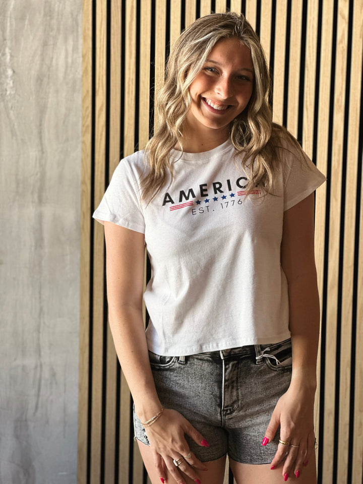 Front picture of model wearing America EST 1776 Crop Top in white with navy and red writing