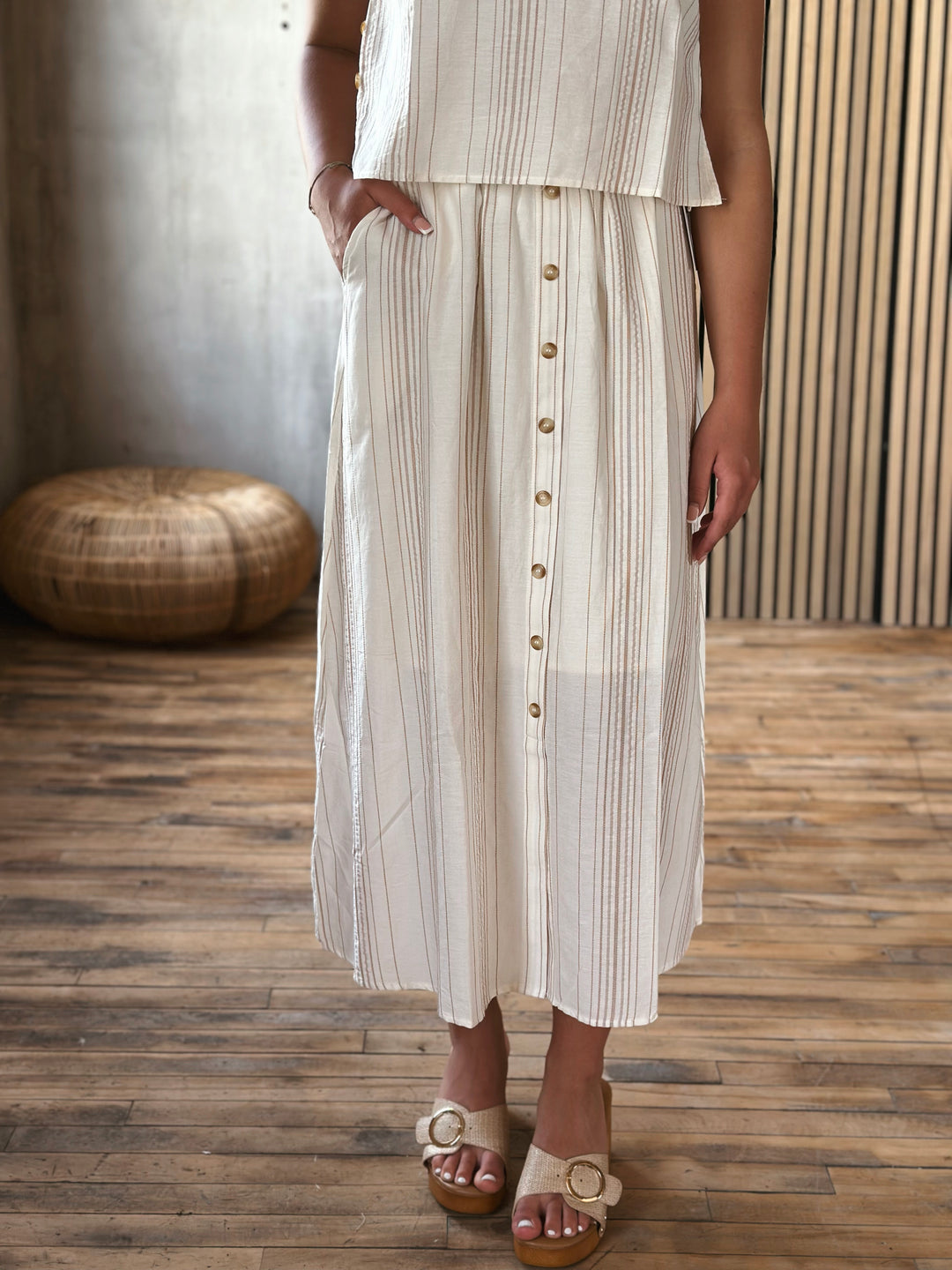 Person wearing a white and beige striped outfit with buttons on a wooden floor.