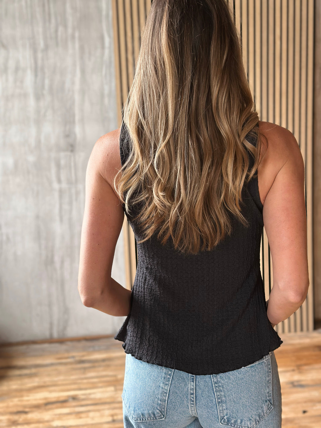 A person wearing a black sleeveless top and light blue jeans with a neutral background.