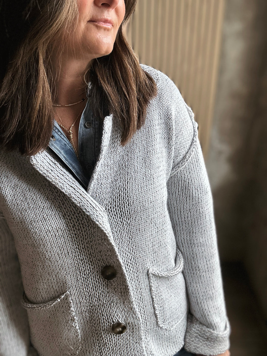 Person wearing a gray knitted cardigan with a blurred background