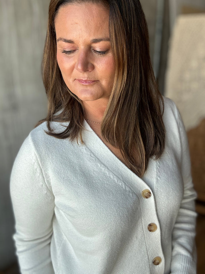 A woman wearing a white knit cardigan with brown buttons.