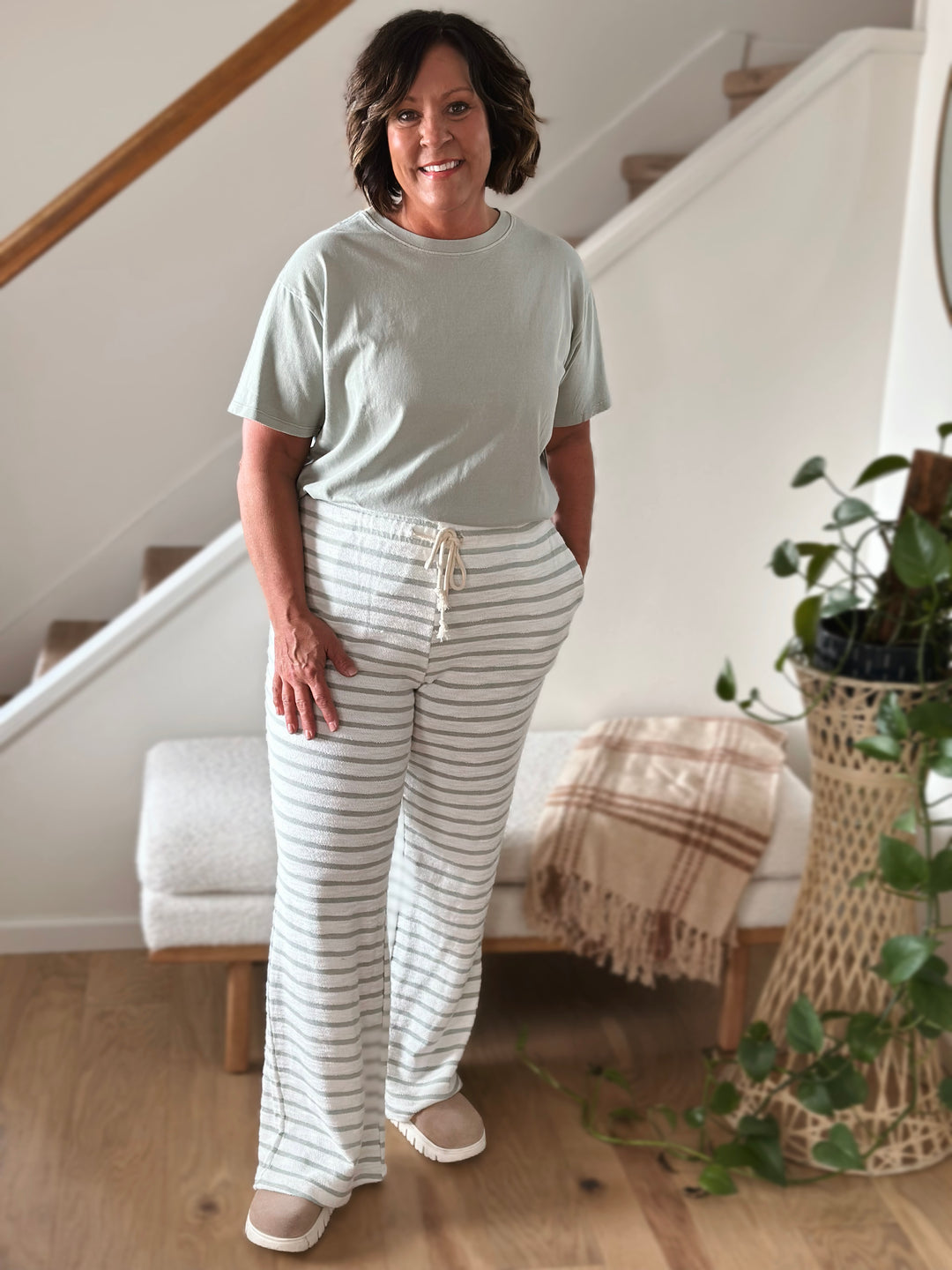 Woman wearing a light gray t-shirt and white and sage striped pants looking forward