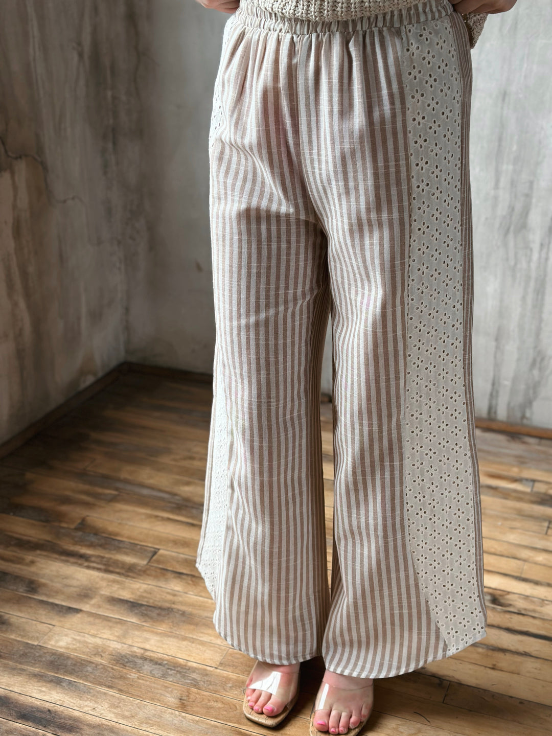Person wearing beige striped pants standing on a wooden floor with a neutral wall background