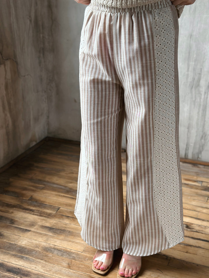 Person wearing beige striped pants standing on a wooden floor with a neutral wall background