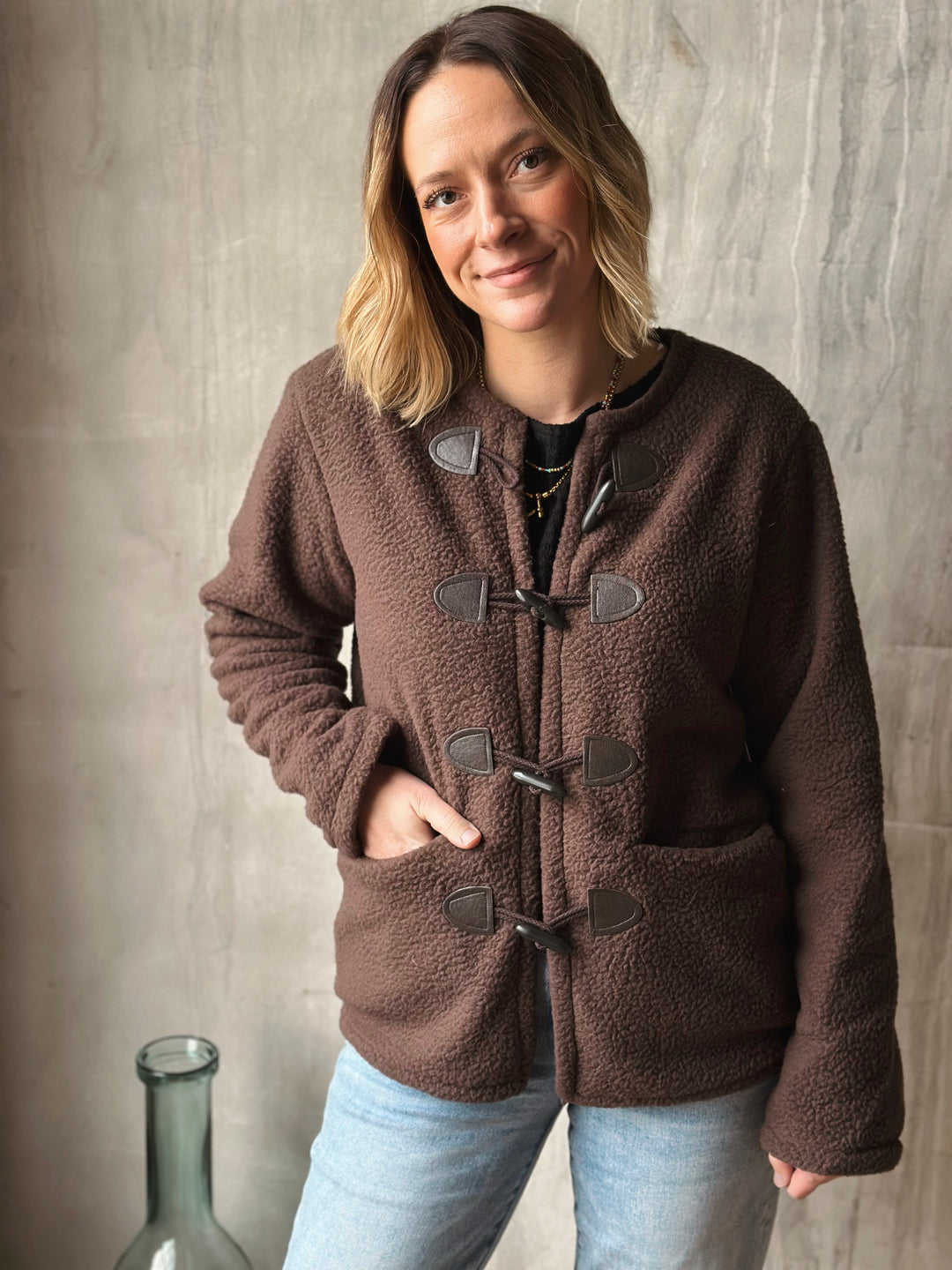 Woman wearing a brown fleece jacket with duffle coat style against a neutral background