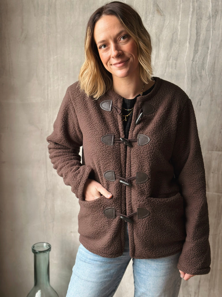 Woman wearing a brown fleece jacket with duffle coat style against a neutral background