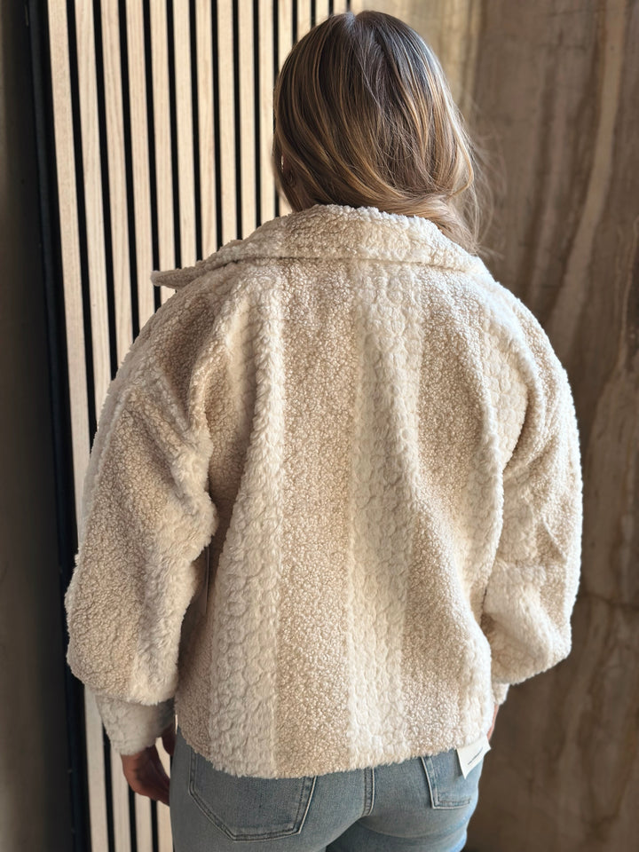 Person wearing a beige textured jacket standing against a neutral wall.