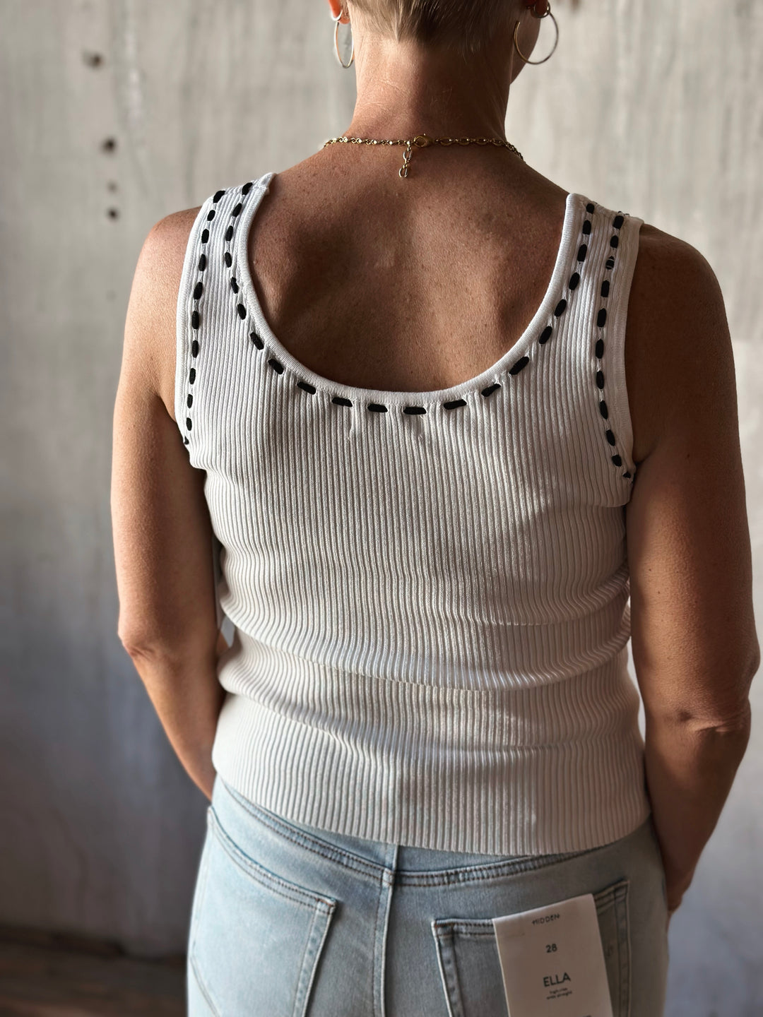 back view of sleeveless sweater knit tank features a flattering scoop neckline and a playful front tie detail. Cream top with black bow. 