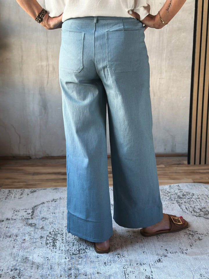 Person wearing light blue wide-leg pants standing in a room with a neutral background.