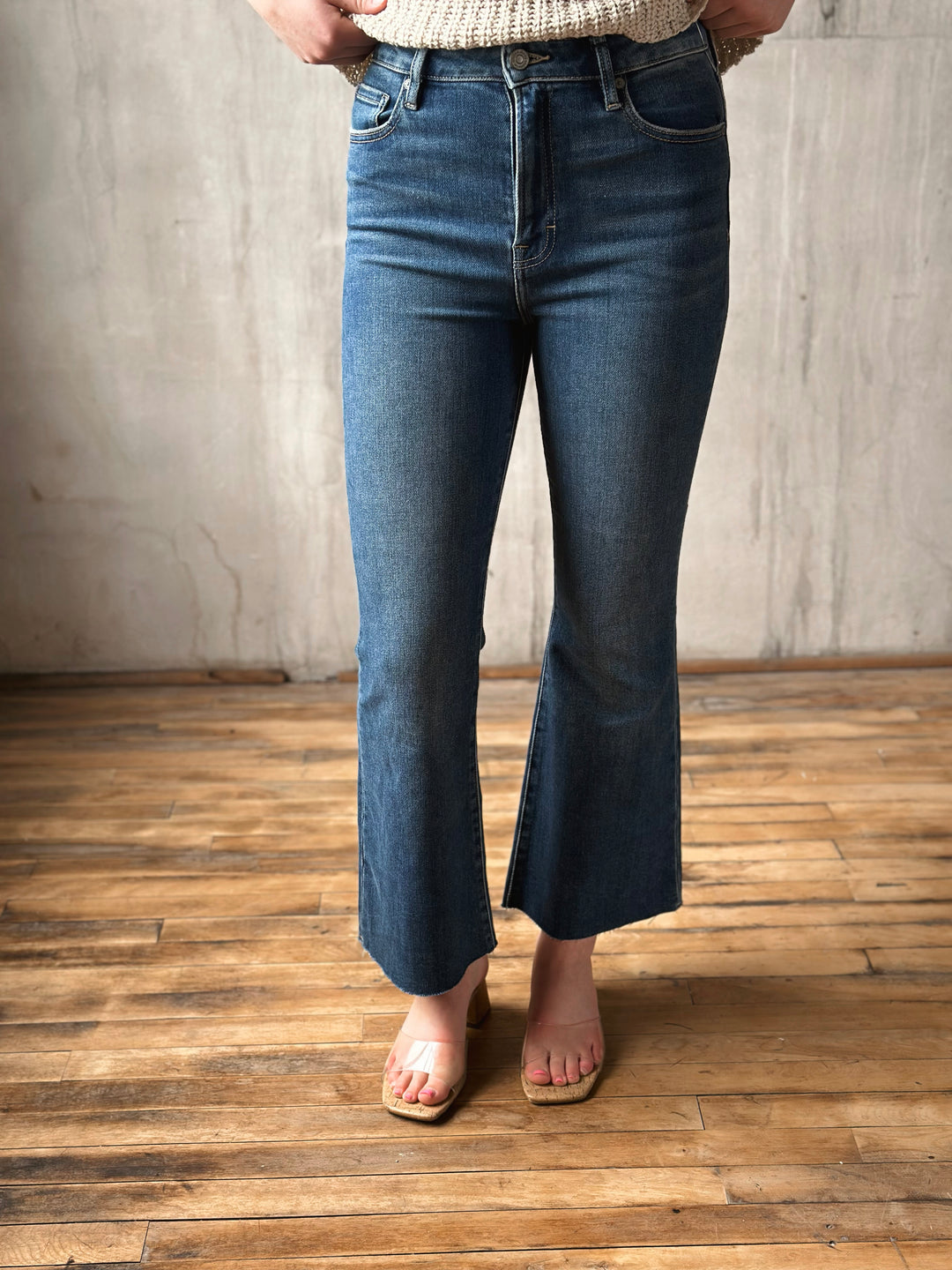 Person wearing blue flared jeans standing on a wooden floor with a neutral wall background