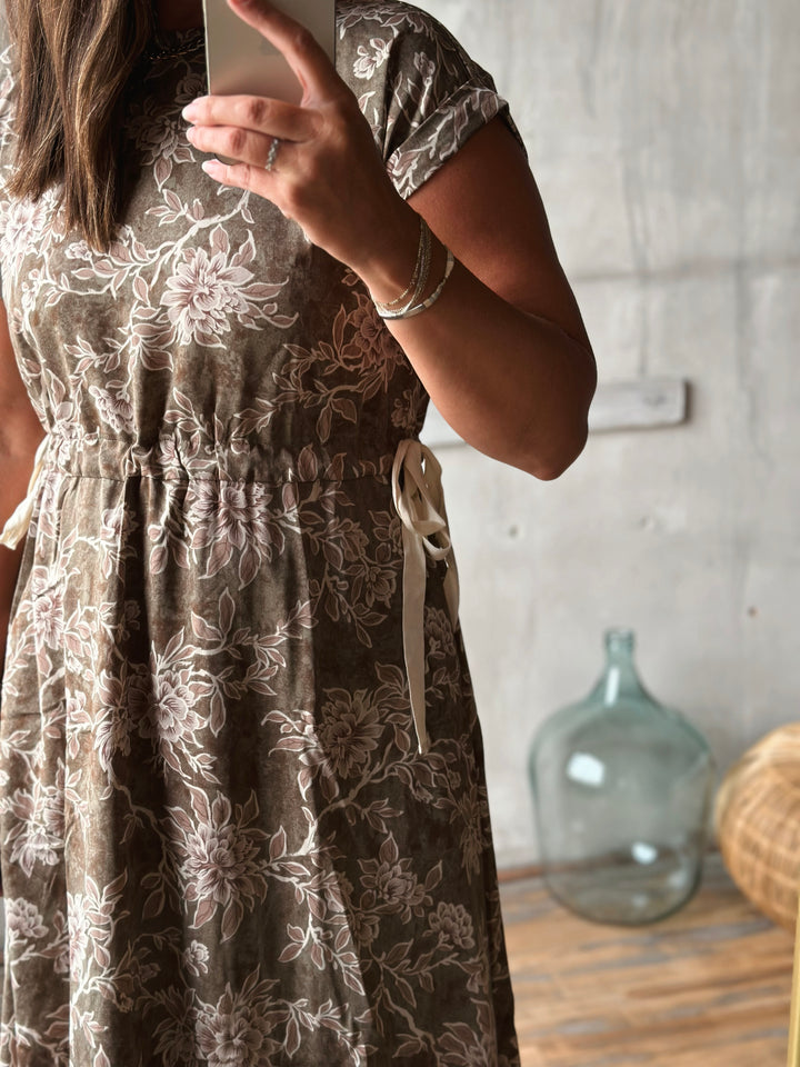 Person wearing a floral dress taking a selfie in a room with a decorative bottle in the background.
