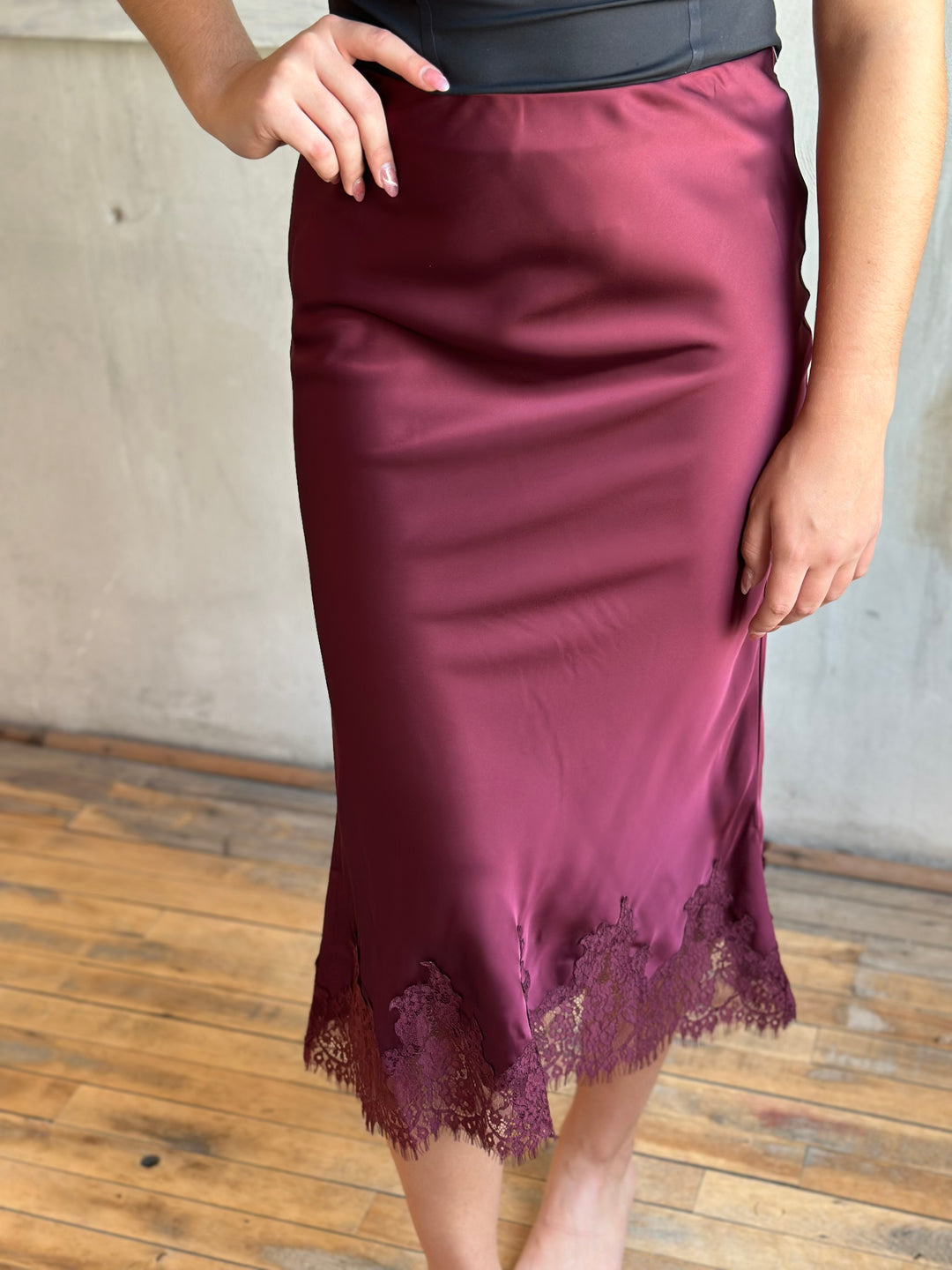 Burgundy satin midi skirt with a lace-trimmed hem, close-up