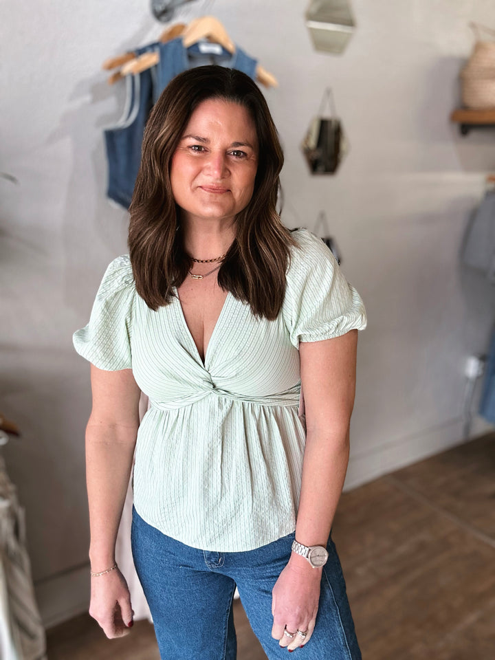 Woman wearing a light green top with a knot detail and blue jeans in a clothing store.