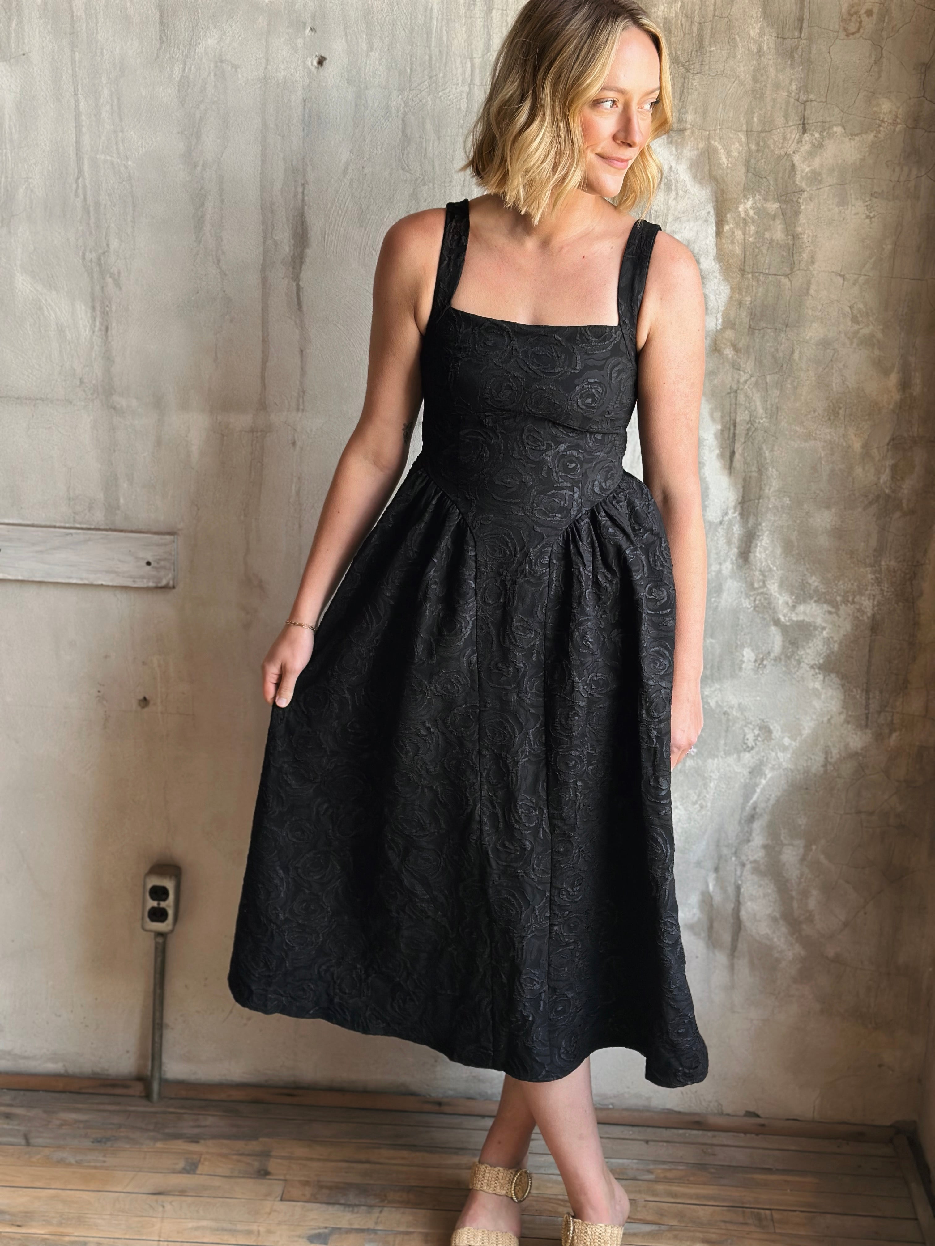 Woman wearing a black dress standing against a textured wall.