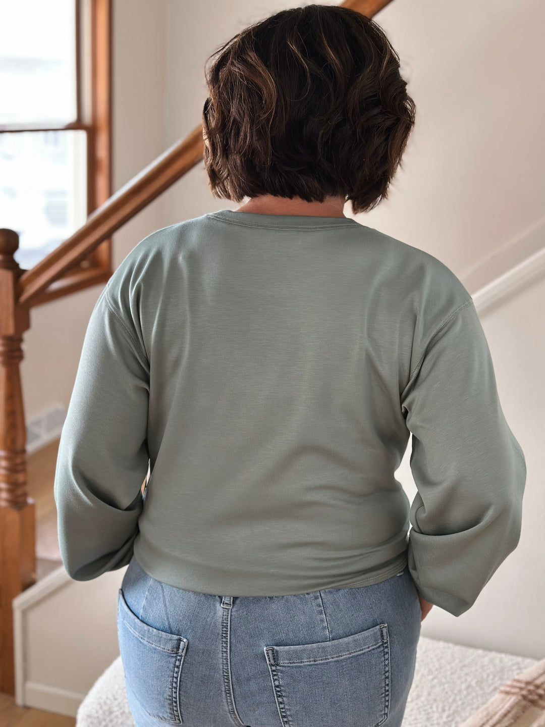 Person wearing a green sweatshirt and blue jeans standing on a staircase.