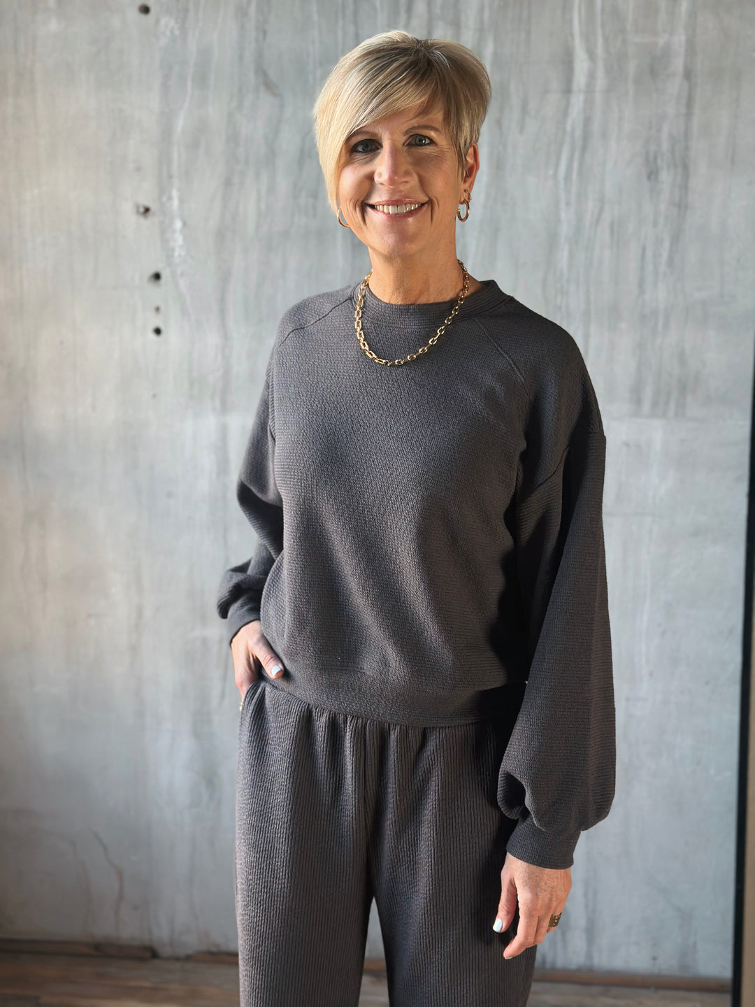 Woman wearing a dark gray sweater and pants against a neutral background