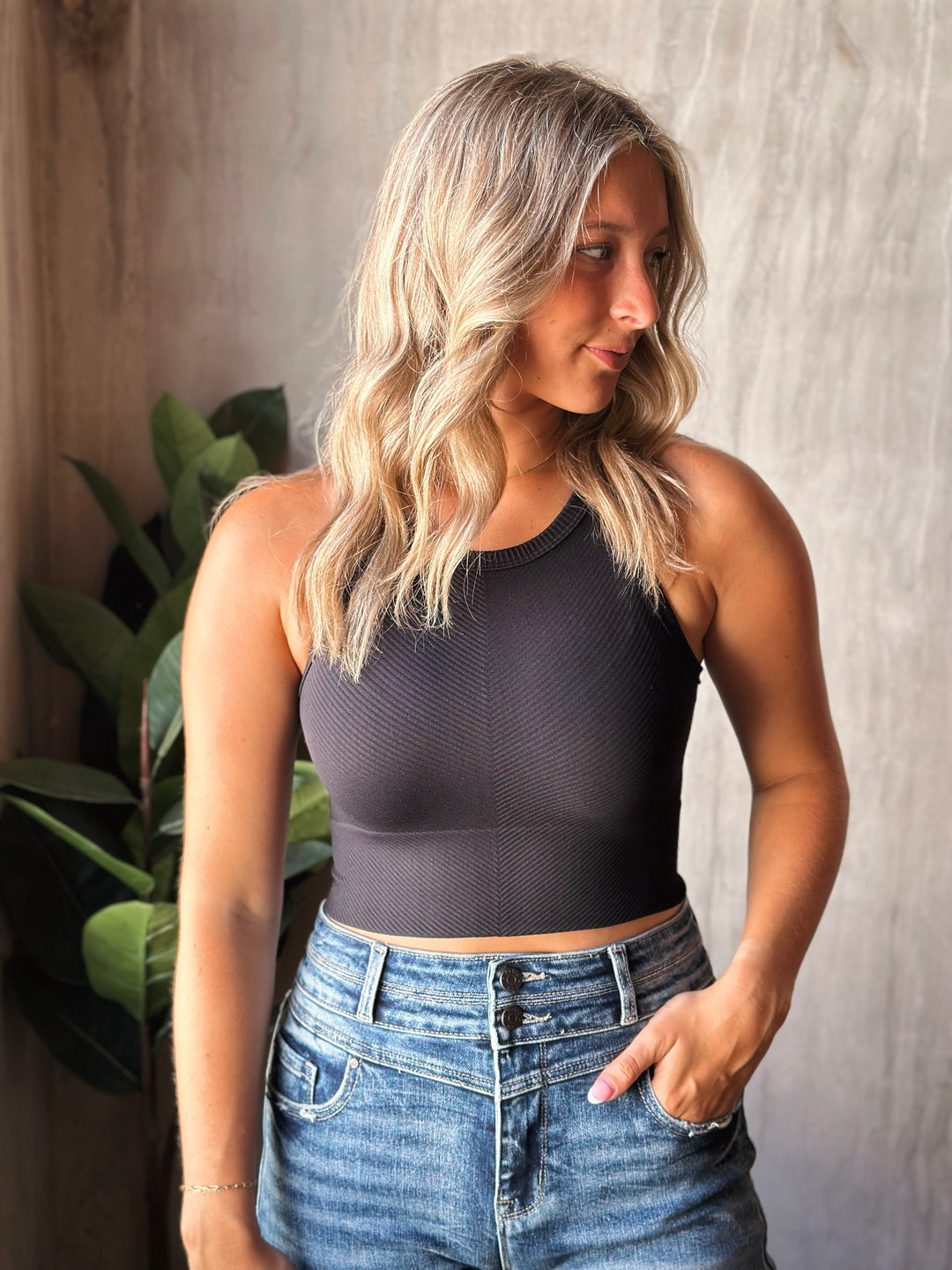 Woman wearing a black sleeveless top and blue jeans against a neutral background
