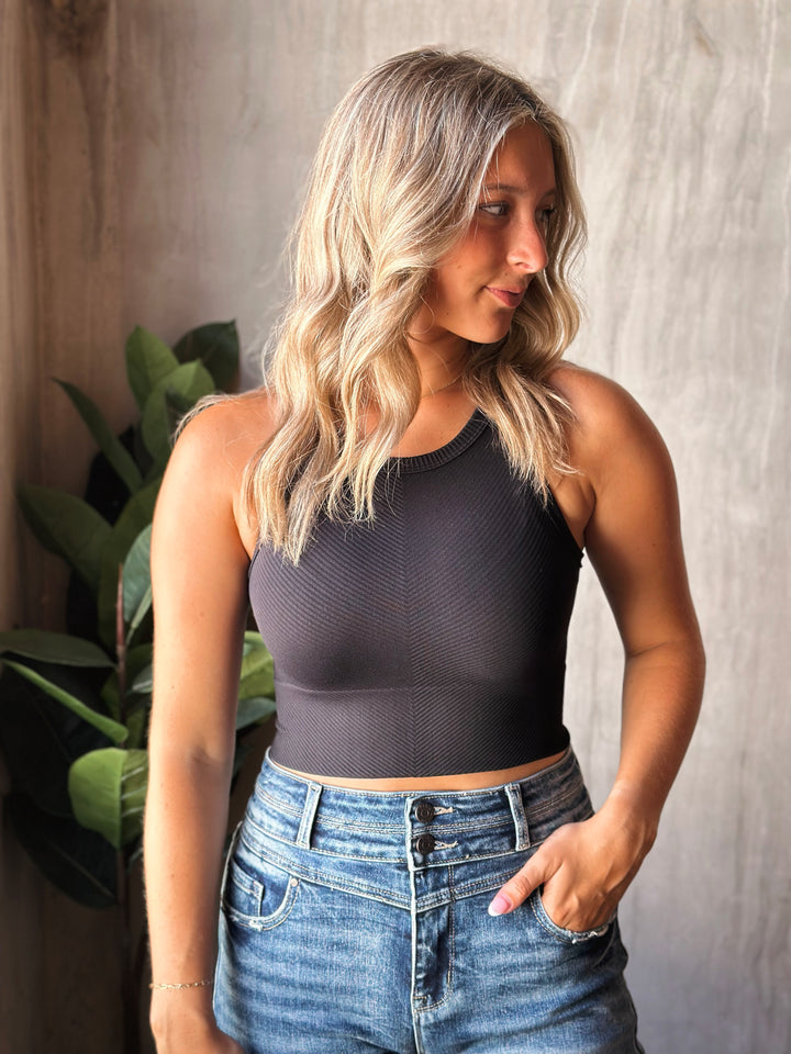Woman wearing a black sleeveless top and blue jeans against a neutral background