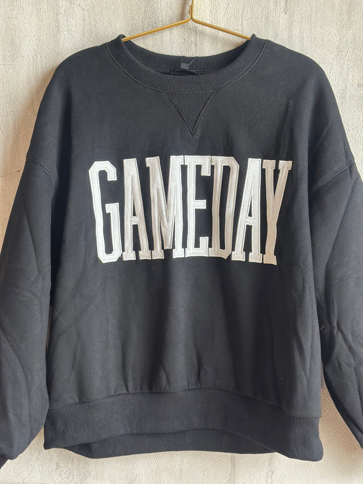 A dark gray crewneck sweatshirt hanging on a wooden hanger against a textured off-white wall. The sweatshirt features the word &
